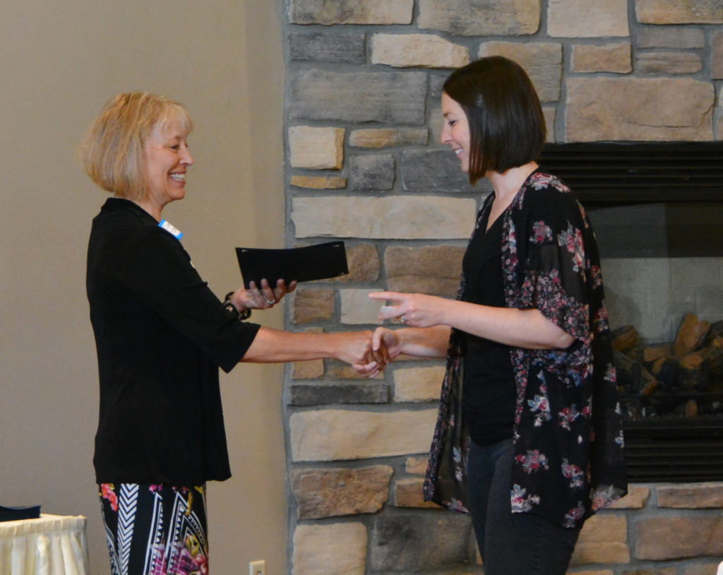 Two women shake hands as one offers the other a certificate - McLeod County Leadership