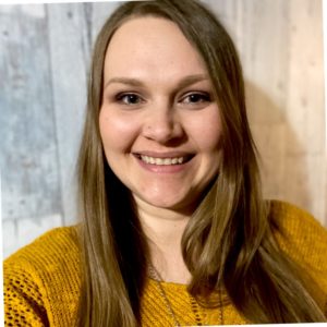 A head shot of Meg wearing a golden sweater and necklace